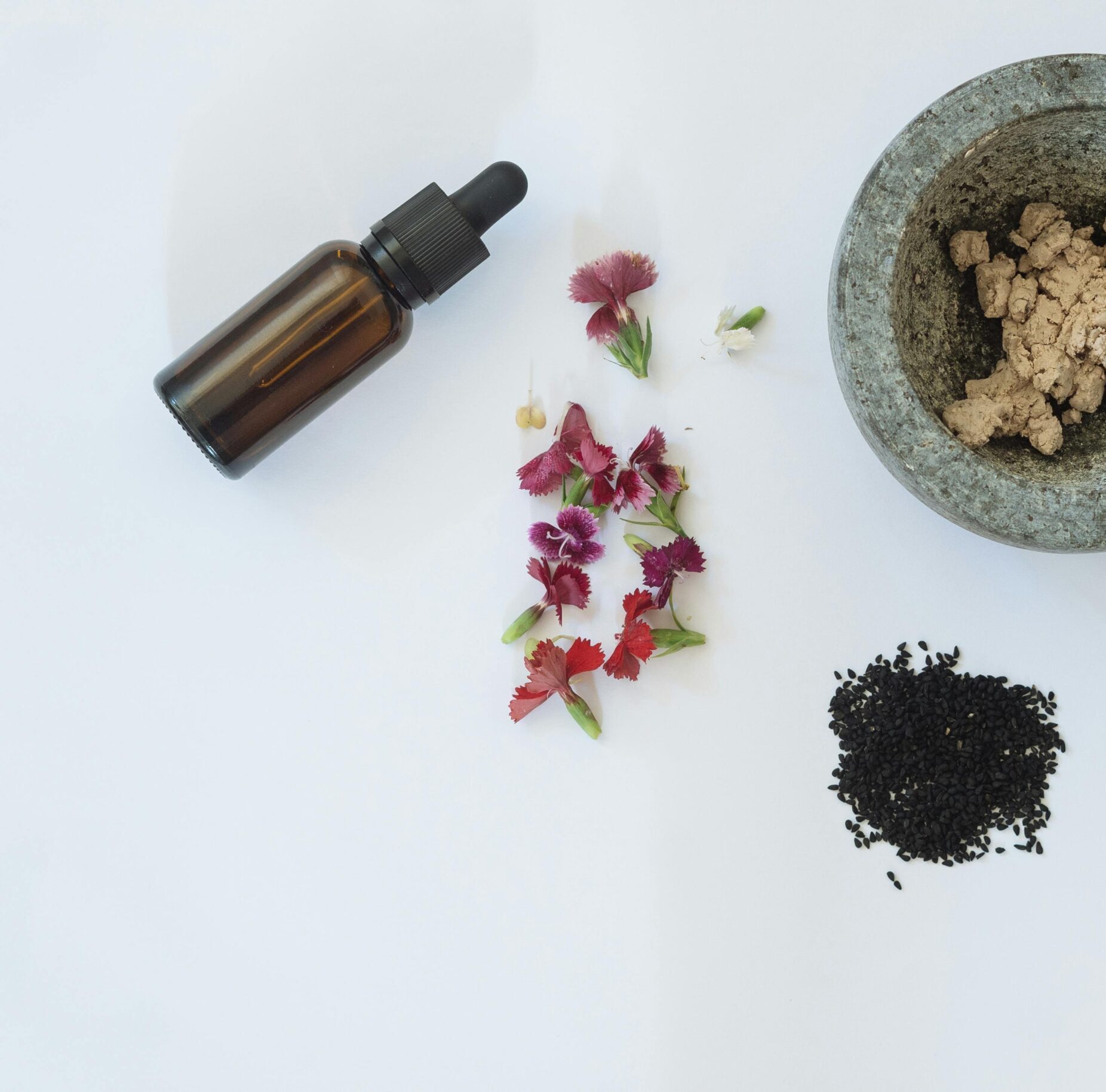 Flat lay of natural skincare ingredients including flowers, black seeds, and a dropper bottle.